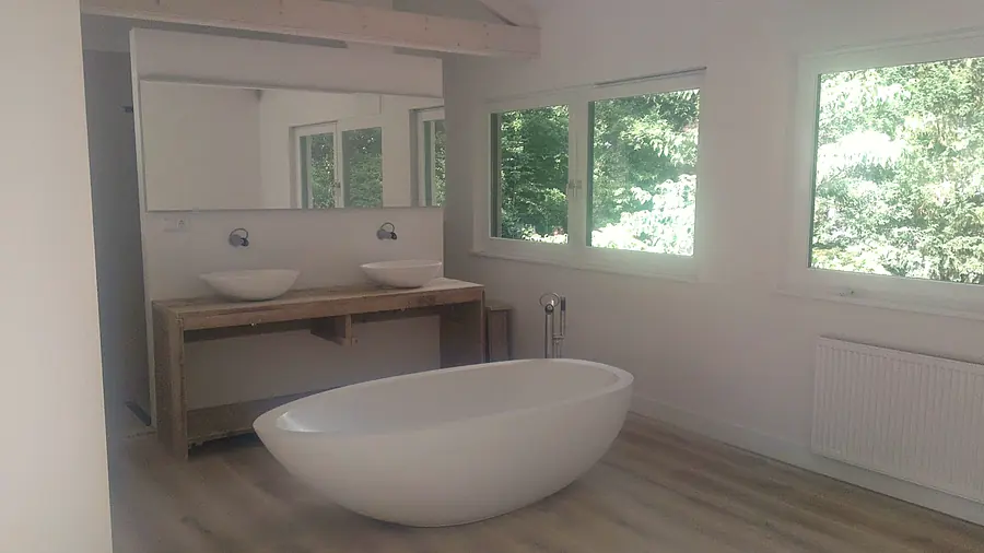 Badkamer met vrijstaand bad, dubbele wastafel en uitzicht op de tuin