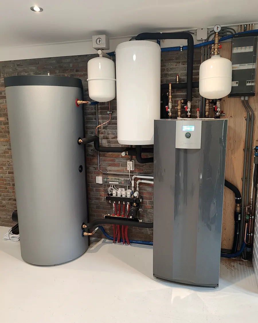 Bodemwarmtepomp met buffervat, boiler en expansievaten in een bijkeuken met bakstenen wand