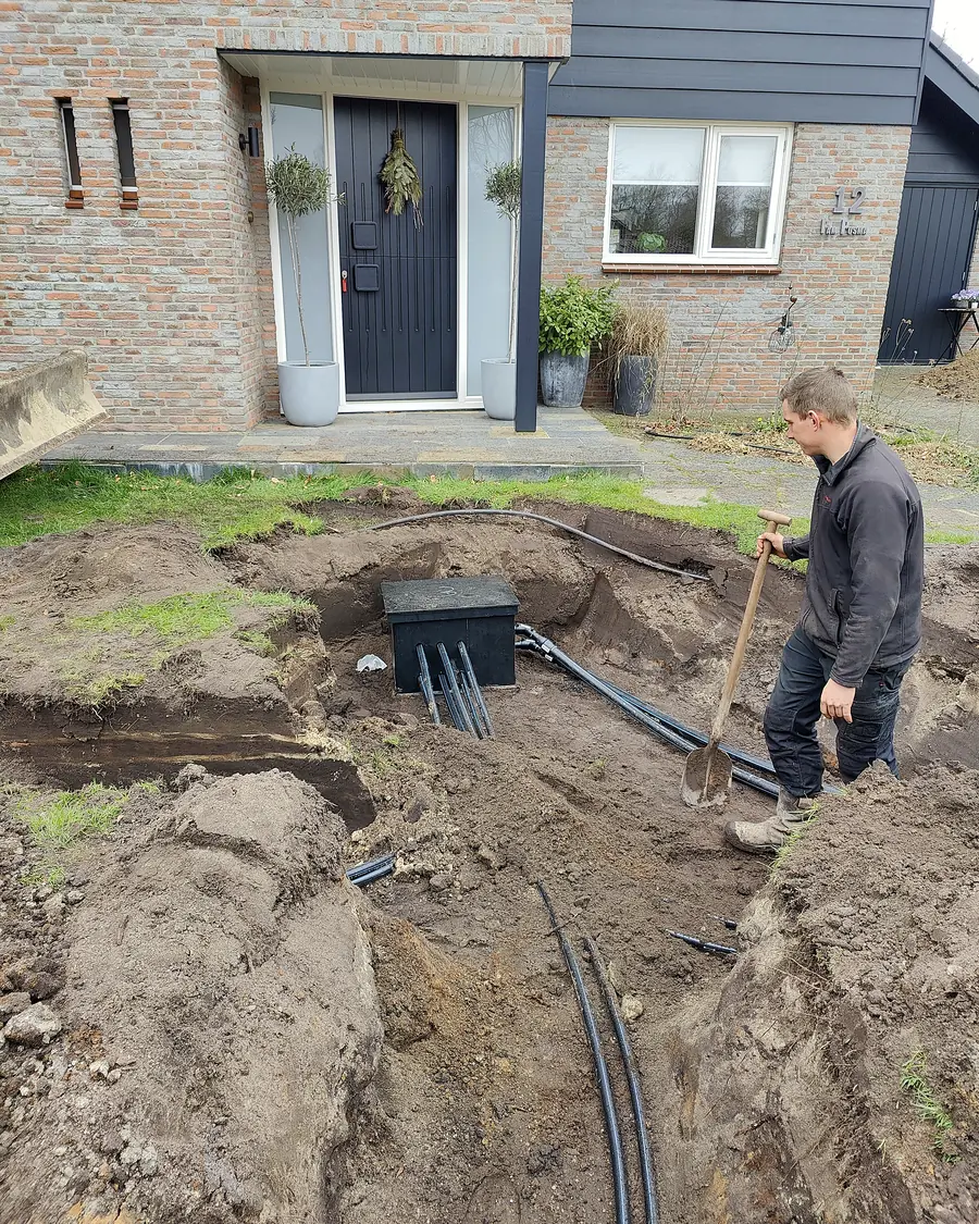 Monteur legt de leidingen van een bodemlus in de sleuf naast een woning