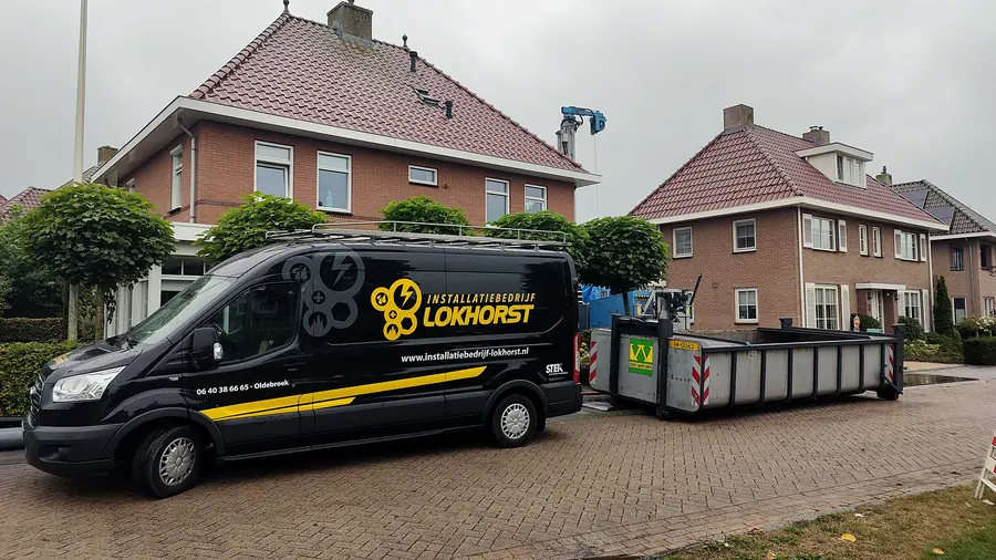 De bedrijfsbus van Installatiebedrijf Lokhorst bij een woning, met de boorstelling voor de bodemlus ernaast