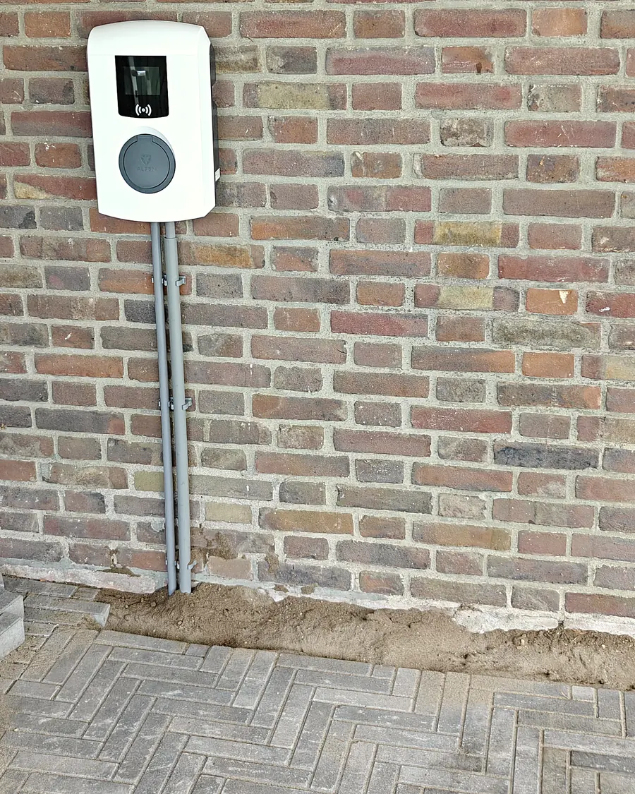 Laadpaal aan de bakstenen wand onder een carport, met visgraatbestrating