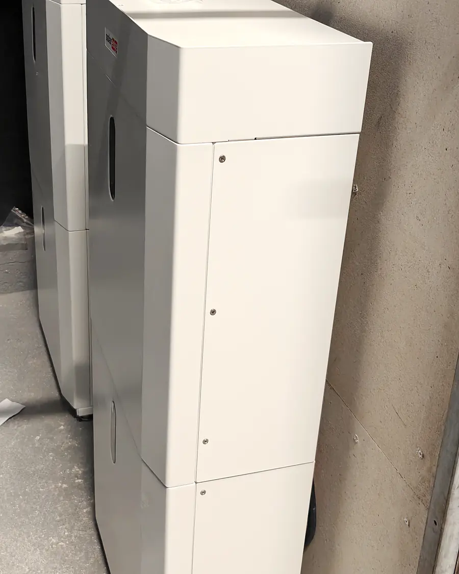 Twee torens van gestapelde thuisbatterijmodules tegen een betonnen wand