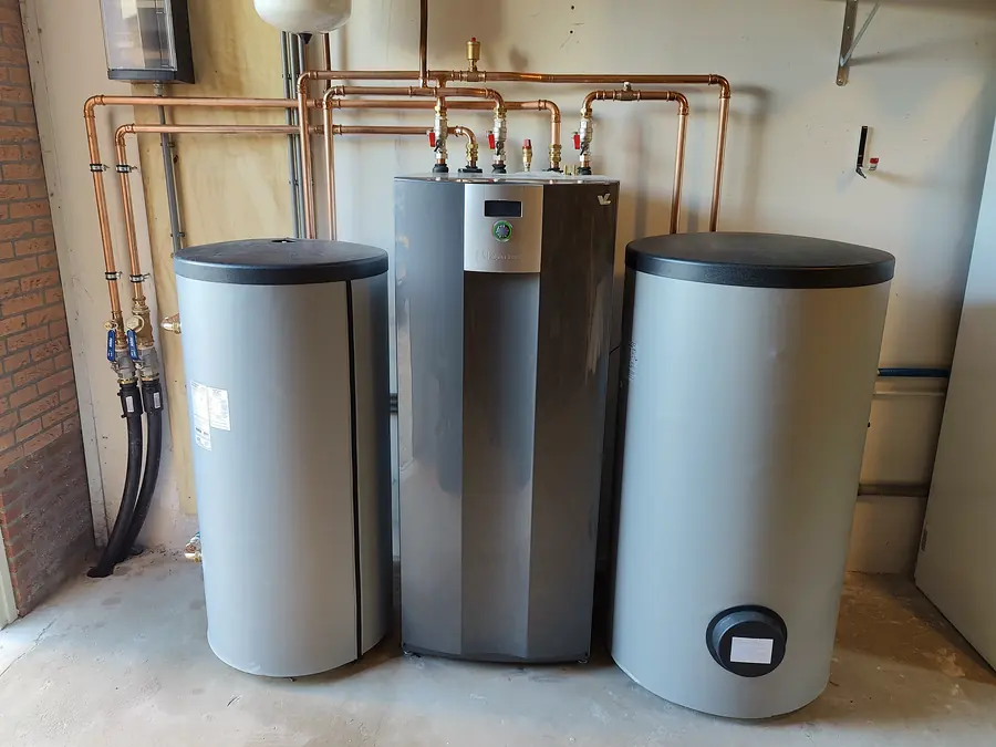 Bodemwarmtepomp met buffervat en boiler in een technische ruimte, met koperen leidingwerk erboven