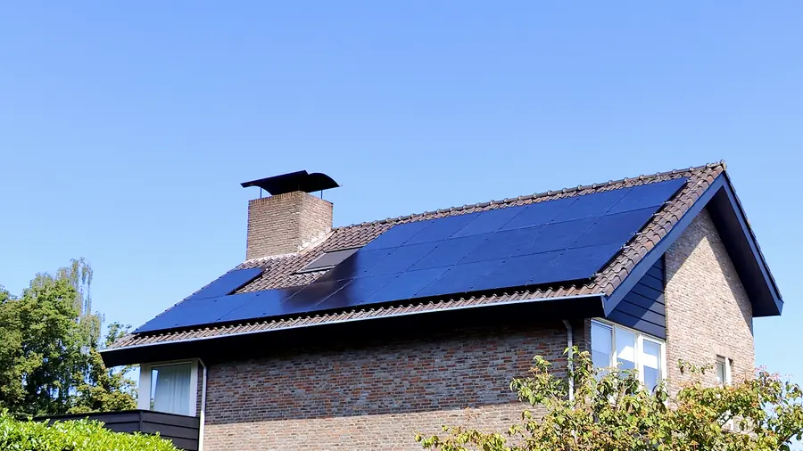 Zwarte zonnepanelen op een donker pannendak tegen een strakblauwe lucht